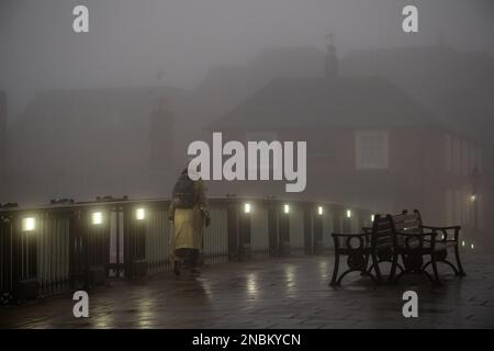 Windsor, Berkshire, Großbritannien. 14. Februar 2023. Eine Frau geht bei Sonnenaufgang über die Windsor Bridge. Es war ein nebiger Start in den Tag in Windsor, Berkshire. Eine Warnung des MET Office Gelb wegen Nebel bleibt bis heute Morgen um 10am Uhr in London und Südostengland bestehen. Kredit: Maureen McLean/Alamy Live News Stockfoto