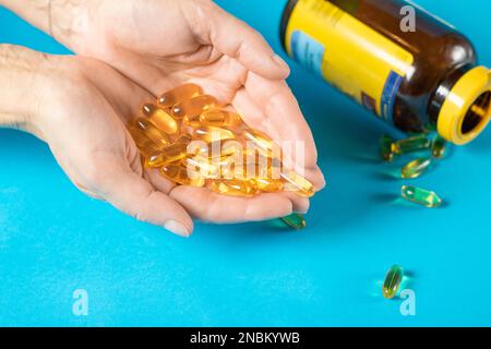 Kapseln mit Fischöl liegen in weiblichen Handflächen auf blauem Hintergrund Stockfoto