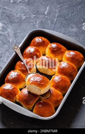 Hawaiianische süße Brötchen, portugiesisches süßes Brot, weiche und dehnbare Brötchen in Backform auf Betontisch mit Zutaten, vertikale Ansicht Stockfoto