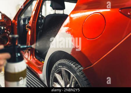 Der Mann poliert mit einem Spray die Karosserie mit einem Putz und bereitet das Auto für die Lackierung vor. Hochwertige Fotos Stockfoto