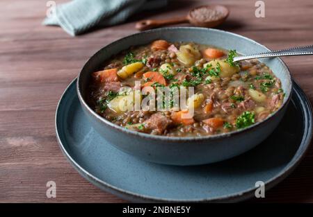 Linsensuppe oder Eintopf. Mit Gemüse, Kartoffeln und Schweinefleisch isoliert auf einem Holztisch gekocht. Nahaufnahme und Vorderansicht Stockfoto