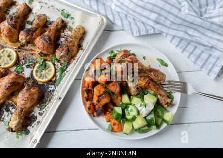 Gebackene Hähnchenschenkel mit Süßkartoffeln und Gurkensalat auf einem Teller Stockfoto