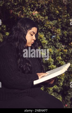 Junge Frau, die im Garten ein Buch liest Stockfoto