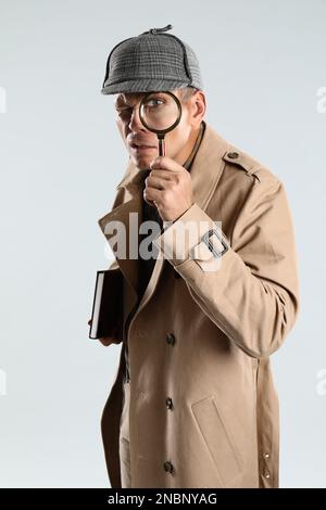 Männlicher Detective, der durch eine Lupe auf grauem Hintergrund schaut Stockfoto