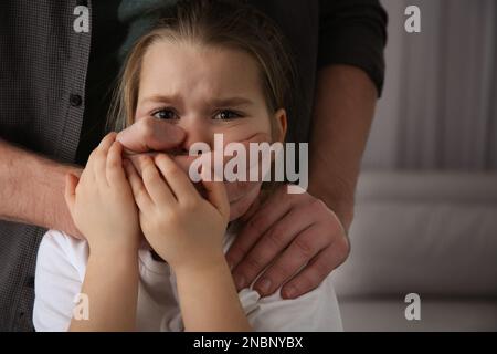 Ein Mann, der den Mund eines verängstigten kleinen Mädchens drinnen verdeckt. Häusliche Gewalt Stockfoto