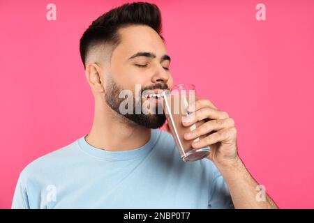 Junger Mann, der Schokoladenmilch trinkt, auf rosa Hintergrund Stockfoto