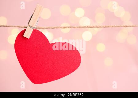 Rotes Herz, das an einem Seil vor festlichen Lichtern hängt, Platz für Text. St. Valentinstag Stockfoto