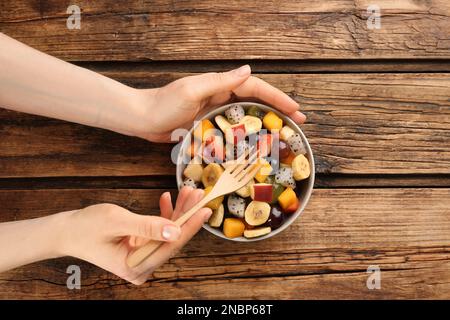 Frau mit köstlichem exotischen Obstsalat am Holztisch, Draufsicht Stockfoto