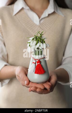 Eine Frau mit einer Vase mit schönen Schneetropfen und einem traditionellen Martisor, Nahaufnahme. Symbol des ersten Frühlingstages Stockfoto