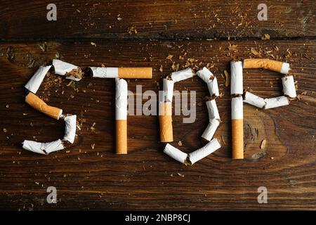 Wort "Stopp der geschnittenen Zigaretten" auf Holztisch, flach liegend. Raucherentwöhnungskonzept Stockfoto