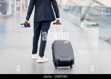 Nicht Wiedererkennbarer Schwarzer Im Anzug, Der Mit Koffer Am Flughafen Spaziert Stockfoto