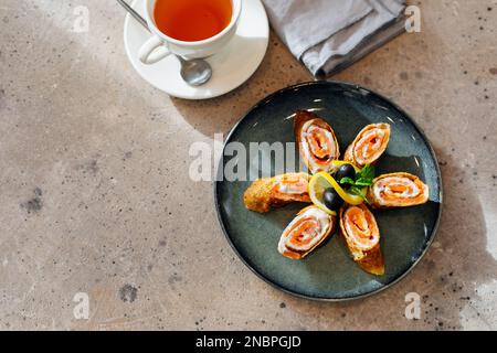 Brötchen mit dünnen Pfannkuchen mit geräuchertem Lachs, Frischkäse und einer Tasse Tee. Köstliches und gesundes Frühstück oder Brunch. Draufsicht Stockfoto