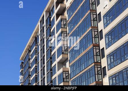 Poltava, Ukraine. Februar 21. 2022. Ein Teil der Fassade eines Wohngebäudes, weiße Wände und Glasbalkone, vor einem blauen Himmel. Stockfoto