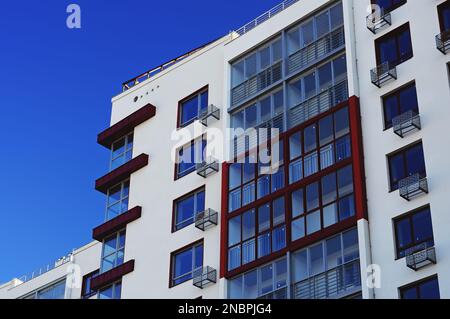 Poltava, Ukraine. Februar 21. 2022. Ein Teil der Fassade eines modernen Appartementgebäudes, weiße Wände und Glasbalkone vor dem blauen Himmel. Stockfoto