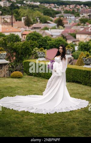 Elegante schwangere Frau in wunderschönem weißen Kleid, die draußen spaziert Stockfoto