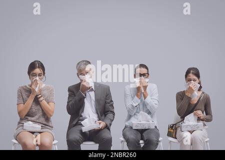 Kranke Menschen mit Erkältung und Grippe sitzen im Warteraum des Krankenhauses und blasen ihre Nase Stockfoto