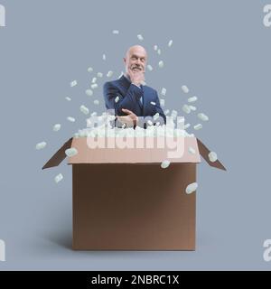 Selbstbewusster lächelnder Geschäftsmann, der mit der Hand am Kinn denkt und aus einer Lieferbox, Geschäftslösungen und einem Kreativitätskonzept herauskommt Stockfoto