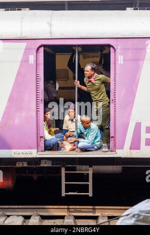 Passagiere in einem offenen Eingang eines Eisenbahnwaggons, der auf die Abfahrt vom Bahnhof Howrah Junction, Howrah, Kalkutta, Westbengalen, Indien wartet Stockfoto