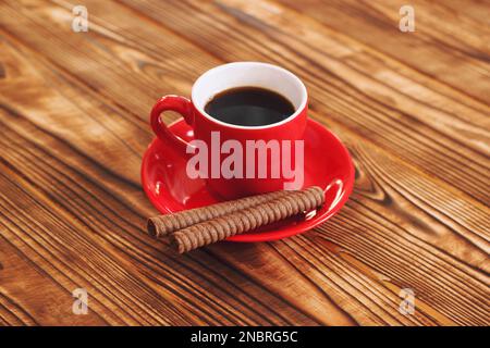 Rote Tasse Heißer Kaffee Auf Einem Holztisch Mit Süßen Schokoladenrohrkugeln. Gemütliches Heim Heißes Getränk Mit Süßigkeiten. Stockfoto