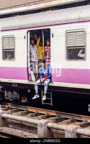 Passagiere in einem offenen Eingang eines Eisenbahnwaggons, der auf die Abfahrt vom Bahnhof Howrah Junction, Howrah, Kalkutta, Westbengalen, Indien wartet Stockfoto