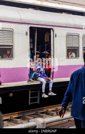 Passagiere in einem offenen Eingang eines Eisenbahnwaggons, der auf die Abfahrt vom Bahnhof Howrah Junction, Howrah, Kalkutta, Westbengalen, Indien wartet Stockfoto