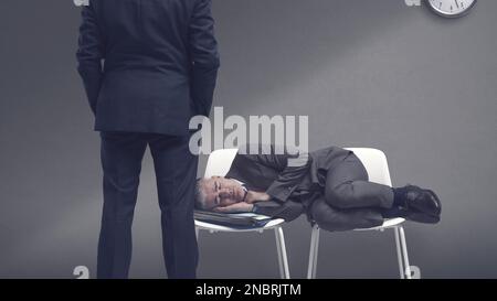 Erschöpfter fauler Geschäftsmann, der auf Stühlen liegt und schläft, sieht ihn sein Chef an Stockfoto