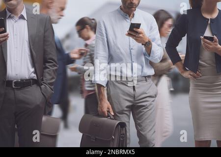 Eine Menge abgelenkter Menschen, die auf der Straße der Stadt laufen und Smartphones benutzen, Internet-Suchtkonzept Stockfoto
