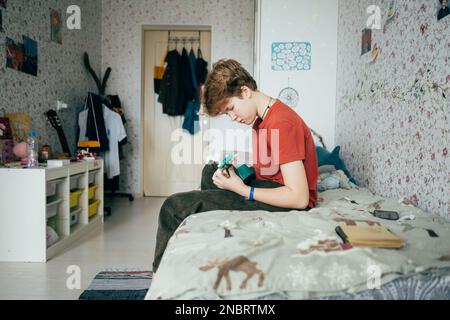 Ein Mädchen im Teenageralter, das auf dem Bett sitzt, lernt Ukulele zu spielen. Stockfoto