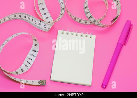 Leeres offenes Notizbuch mit Zentimeterband auf rosa Hintergrund mit Platz für Text oder Business Food Konzept. Konzept Sport, Diät, Fitness, gesunde Ernährung Stockfoto