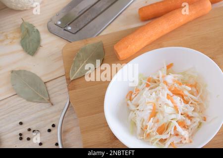 Heim-Sauerkraut mit Karotten und Gewürzen auf einem Teller, Sauerkraut. Gemischter Salat aus frischem Gemüse auf einem Teller mit einer Gabel auf Holzhintergrund. Stockfoto