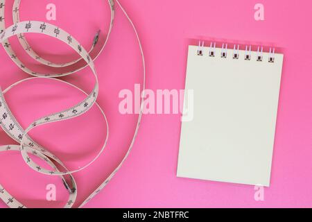 Leeres offenes Notizbuch mit Zentimeterband auf rosa Hintergrund mit Platz für Text oder Business Food Konzept. Konzept Sport, Diät, Fitness, gesunde Ernährung Stockfoto