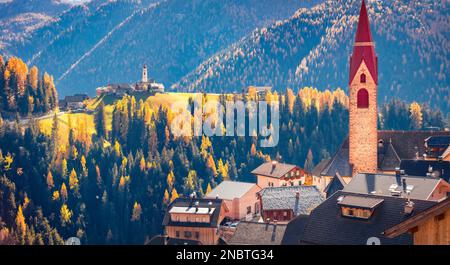 Farbenfroher Herbstblick auf die Glocke der christlichen Kirche Pfarrei Maria vom Guten Rat mit der katholischen Kirche Dlijia Da Curt im Hintergrund, Italien, Europa. Reisen Stockfoto