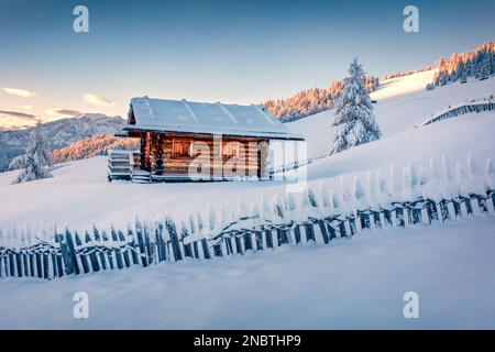 Unberührte Winterlandschaft. Hölzernes Chalet auf dem Hügel des Dorfes Alpe di Siusi. Herrlicher Sonnenaufgang im Winter in den Dolomiten. Herrliche Landschaft der Skigebiete Stockfoto