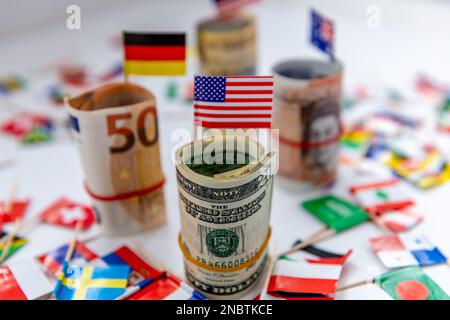 Zusammengerollte Bündel wichtiger Währungen und Landesflaggen mit der US-Dollar- und der amerikanischen Flagge davor. Dollar-Hegemoniekonzept. Stockfoto