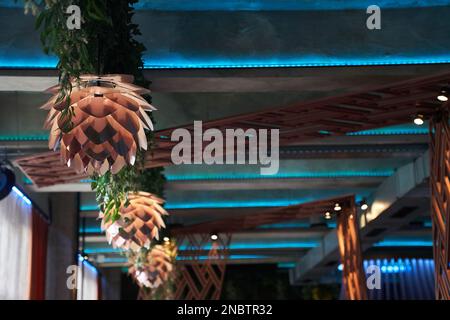 Eine Reihe von Kronleuchtern in Form von Lotusblumen, die von der Decke hängen und von Licht beleuchtet werden. Das Konzept der Inneneinrichtung im Restaurant. Mit Platz zum Kopieren. Hochwertiges Foto Stockfoto