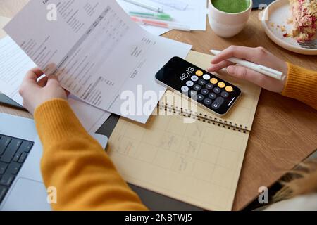 Ein hohes Maß an Erntegut, eine nicht erkennbare Frau, die Finanzunterlagen überprüft und ihr persönliches Geld verwaltet, während sie in einem Café sitzt und sich amüsiert. Stockfoto