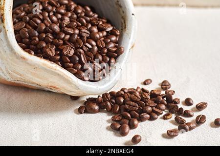 Verschüttete Kaffeebohnen aus Keramik auf Textil background.selective FOCUS Stockfoto