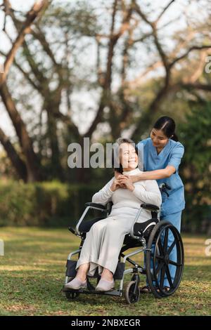 Ältere asiatische Seniorin im Rollstuhl mit Krankenschwester. Pflegeheim Krankenhaus-Garten-Konzept. Stockfoto