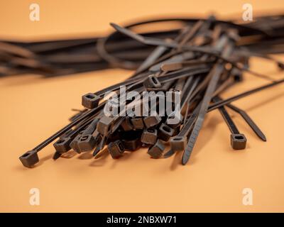 Schwarze Kunststoff-Kabelbinder auf orangefarbenem Hintergrund. Nahaufnahme. Stockfoto