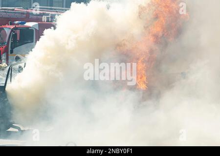 Starke Flammen von brennendem Auto auf dem Hintergrund eines Löschfahrzeugs. Ausbildung der Feuerwehrleute Stockfoto