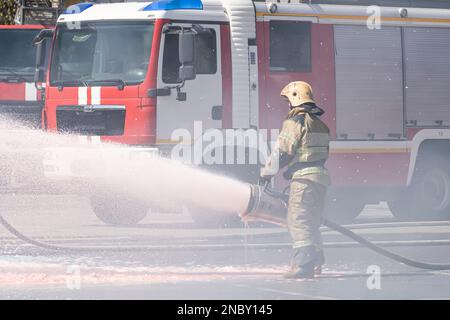 Feuerwehrleute löschen ein Feuer aus einem Löschfahrzeug. Starker Wasser- und Schaum-Durchfluss aus dem Feuerwehrschlauch in der Hand des Feuerwehrmanns. Feuer löschen mit Stockfoto