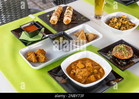 Eine Nahaufnahme verschiedener indischer Gerichte auf einem weißen Tisch mit grüner Tischdecke Stockfoto