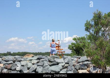 Eine mittelalterliche Künstlerin wird Teil der Landschaft und der Wasserlandschaft, die sie entlang der Anlegestelle der Ostküste malt Stockfoto