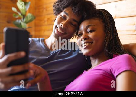 Glückliches afroamerikanisches Paar, das Zeit mit dem Smartphone in einer Blockhütte verbringt. Blockhütte, Natur- und Lifestyle-Konzept. Stockfoto