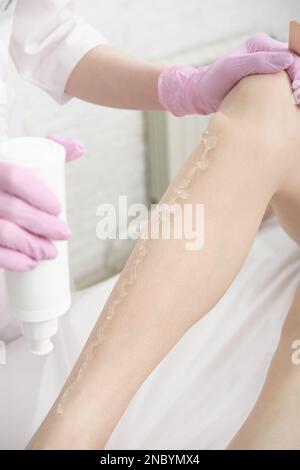 Kosmetikerin, die Führungsgel auf die Beine des Kunden aufträgt. ipl-Laserepilierung. Glatte Haut im Salon. Vertikale Größe. Stockfoto