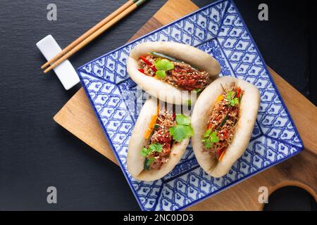 Speisekonzept: Hausgemachte Bao-Brötchen aus biologischem Rind oder Gua Bao auf der quadratischen Platte auf schwarzem Hintergrund mit Kopierbereich Stockfoto