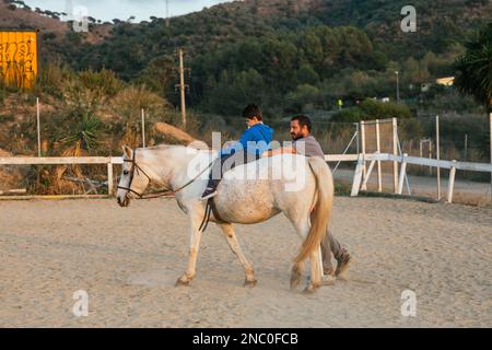 Ein Junge mit Behinderung, der eine Pferdetherapie im Reitzentrum macht. Stockfoto