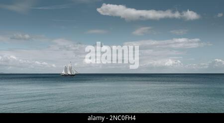 Altes hölzernes Großschiff mit weißen Segeln, die an einem windigen Tag den Ozean überqueren Stockfoto