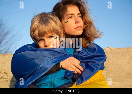 Traurige junge Frau, 18 Jahre alt, umarmt, unterstützt einen müden Jungen, 6 Jahre alt, mit einer blau-gelben Flagge über den Schultern. Familie, Einheit, Gefühle von D Stockfoto