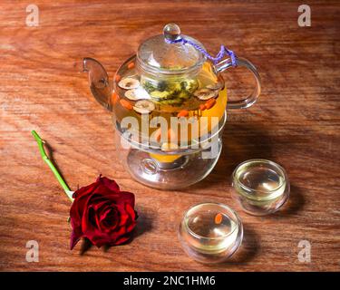 Kamillentee mit Goji-Beeren und Blumen mit Tassen und Rosenblüten auf einem Holztisch Stockfoto